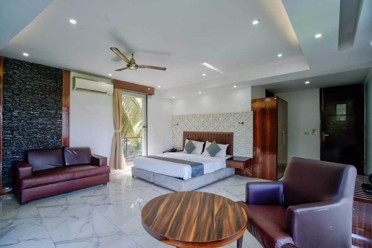 Un dormitorio moderno con cama, sofá, sillón, una mesa redonda de madera y ventilador de techo.