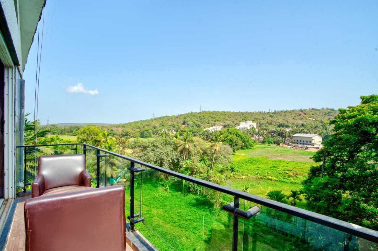A balcony with a chair, a view of a green landscape, and a building in the distance.