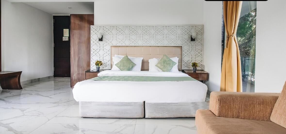 A modern hotel room with a large bed, a sofa, and a view of the outdoors.