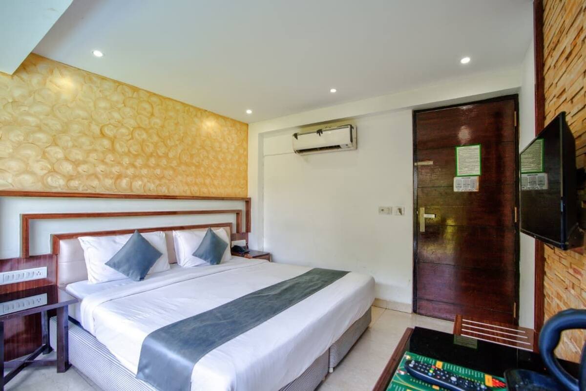 Una habitación de hotel con una cama grande, un cabecero de madera, un televisor de pantalla plana, un equipo de aire acondicionado y una puerta de madera.