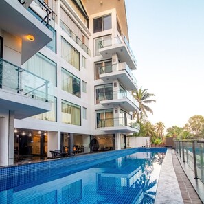 Ett modernt hotell med en swimmingpool, flera balkonger och en fasad av glas.