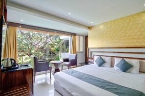 Habitación de hotel con cama, escritorio con hervidor, una silla, una mesita y vistas al exterior con vegetación.