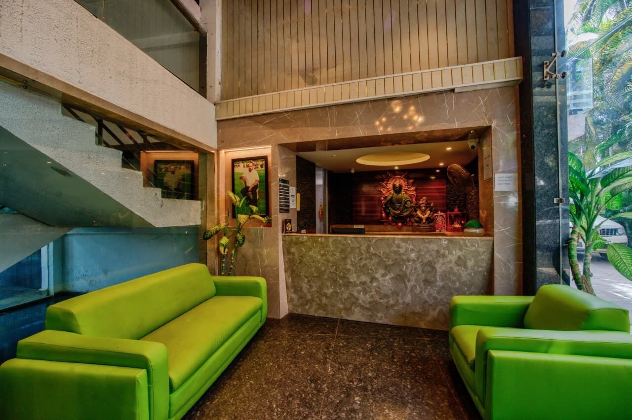 Un vestíbulo con mostrador de recepción, sofás verdes, una escalera y vistas al exterior con vegetación.