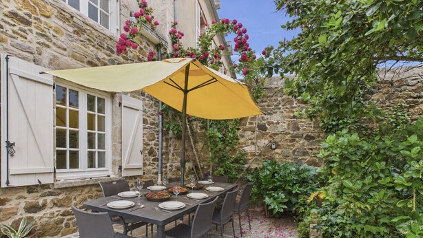 Un espace de restauration en plein air avec un mur en pierre, une table dressée pour quatre personnes et un parasol jaune.