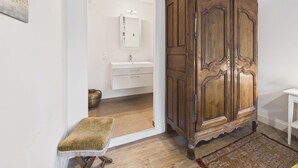 Une armoire en bois, un petit banc et une salle de bain avec un miroir et un lavabo.