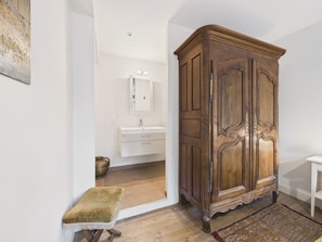 Ein Holzkleiderschrank, eine kleine Bank und ein Badezimmer mit Spiegel und Waschbecken.