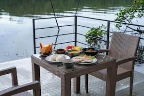 A dining table with food and a chair, set on a dock with a view of water and greenery. - The Aluthgama House by TSC (Dharga Town)