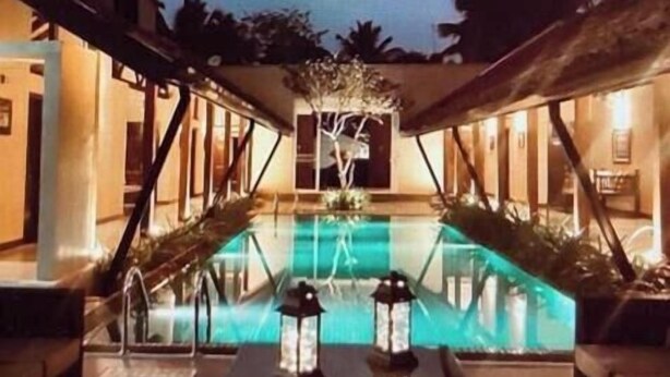 Zona de piscina con una fuente central, dos faroles y un área de descanso con cojines.