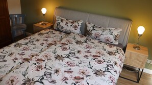 Un dormitorio con una colcha estampada con motivos florales, dos lámparas de noche, una silla y una mesita de noche.