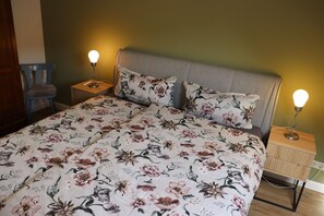 Ein Schlafzimmer mit geblumigter Bettdecke, zwei Nachttischlampen, einem Sessel und einem Nachttisch.