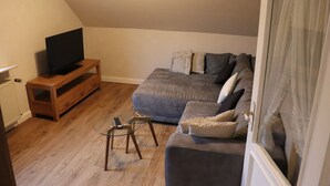 Una sala de estar con un sofá gris, un mueble bajo de televisión de madera y una mesa de centro de cristal.