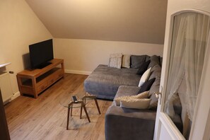 Ein Wohnzimmer mit grauem Sofa, einem HolztV-Schrank und einem Glastisch.