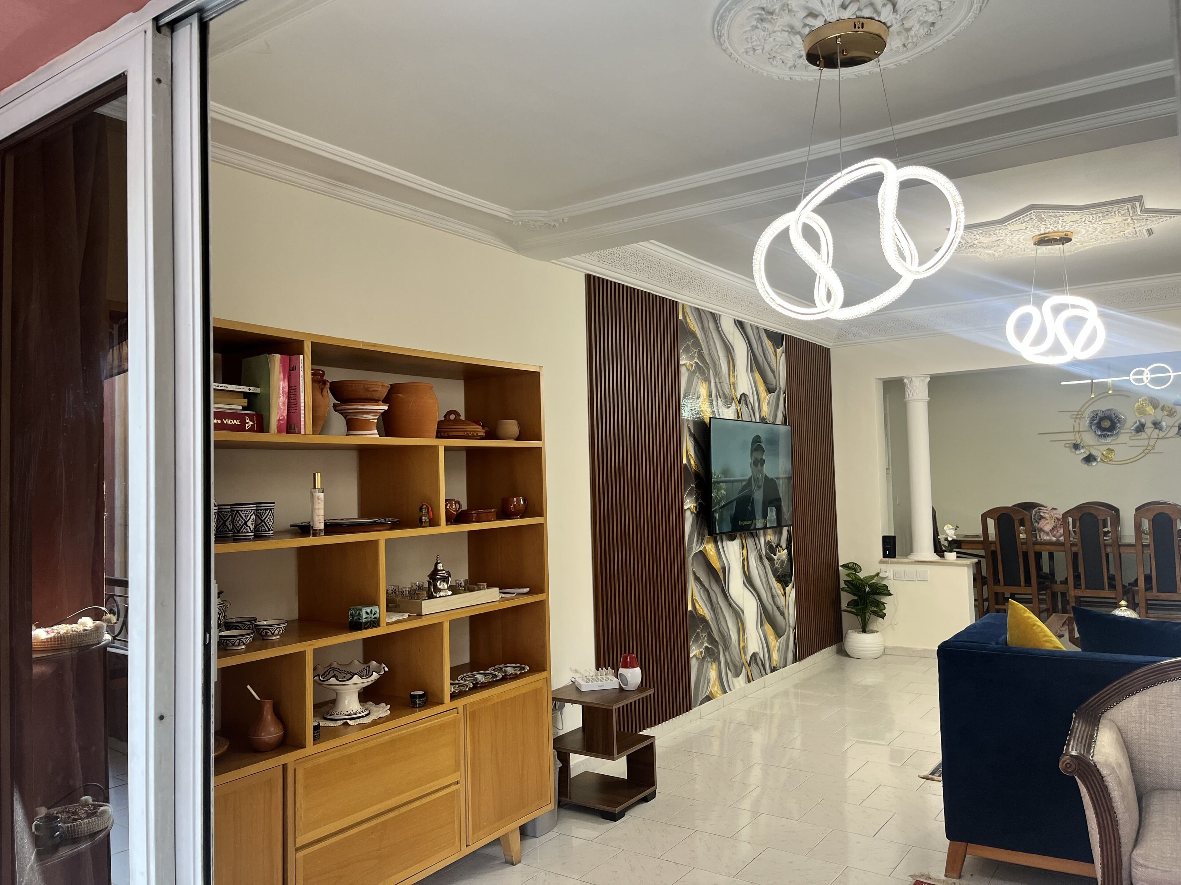 Un salon avec un meuble en bois, un téléviseur fixé au mur, un canapé bleu et un mur à motifs.