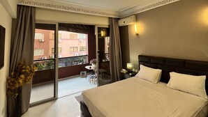 Una habitación de hotel con una cama grande, un balcón que ofrece vistas a edificios y un techo con una lámpara decorativa.