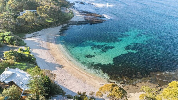 Una propiedad costera con playa, aguas cristalinas y vegetación circundante.