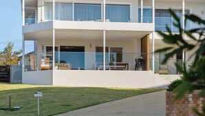 Un edificio moderno de dos pisos con balcones, un espacio de estar al aire libre cubierto y una escalera visible.