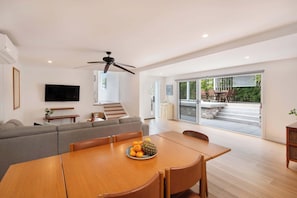 Ein modernes Wohnzimmer mit einer Couch, einem Esstisch mit Obst, einem Fernseher und einem Deckenventilator.