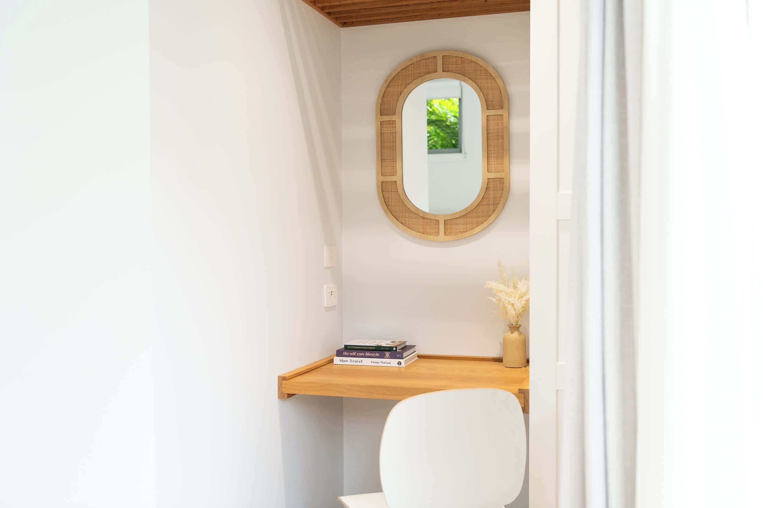 A bathroom with a wooden vanity, a round mirror, and a white chair.