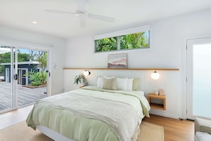 Ein Schlafzimmer mit Bett, Nachttischen, Deckenventilator, Fenster mit Blick und einer Schiebeglastür zu einem Außenbereich.