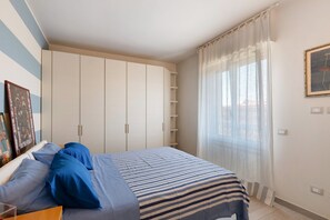 A bedroom with a bed, a wardrobe, a window with curtains, and a framed picture on the wall.