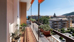 Un balcón con plantas en macetas, vista a un paisaje urbano y cielo despejado.