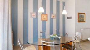 Un comedor con una mesa de vidrio, sillas de metal y una pared a rayas con cuadros.