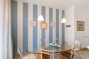 A dining area with a glass table, metal chairs, and a striped wall with framed pictures.