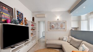 Una sala de estar moderna con televisor de pantalla plana, mueble blanco para equipo audiovisual, sofá beige y una obra de arte en la pared.