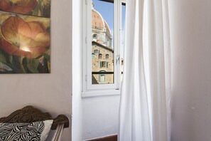 Ein Zimmer mit einem Bett, einem Fenster mit Blick auf ein Gebäude mit einer Kuppel und einem Gemälde an der Wand.