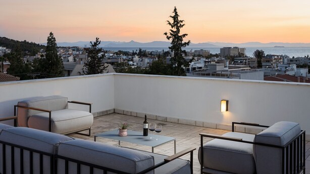 Terraço no telhado com área de estar ao ar livre, uma mesa e uma garrafa de vinho.