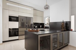 A modern kitchen with built-in appliances, a central island, and a decorative piece on the counter. - Thea House Athenian Riviera (Voula)