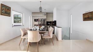 Uma sala de jantar moderna com uma mesa posta para quatro pessoas, uma cozinha ao fundo e obras de arte nas paredes.