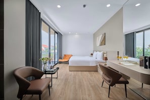 Habitación de hotel moderna con una cama, dos sillones, un escritorio y vistas a la ciudad.