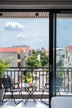 Un balcón con una mesa, sillas, una planta en maceta y vistas a edificios y árboles.