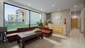 A modern reception area with a reception desk, a seating area with a sofa and a coffee table, and a view of the outside. - Anh Anh Hotel Ninh Binh (Hoa Lu)