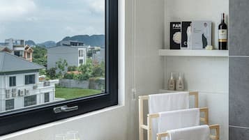 A modern bathroom with a large window, a bathtub, a shelf with toiletries, and a tray with fruit and glasses.