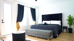 A bedroom with a bed, a small bedside table, a potted plant, a round stool, and a window with curtains. - Wonderful 4-bedroom townhome with AC in vibrant Dallas (Dallas)