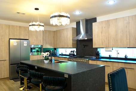 A modern kitchen with wooden cabinets, a central island with bar stools, stainless steel appliances, and pendant lighting.. Wonderful 4-bedroom townhome with AC in vibrant Dallas