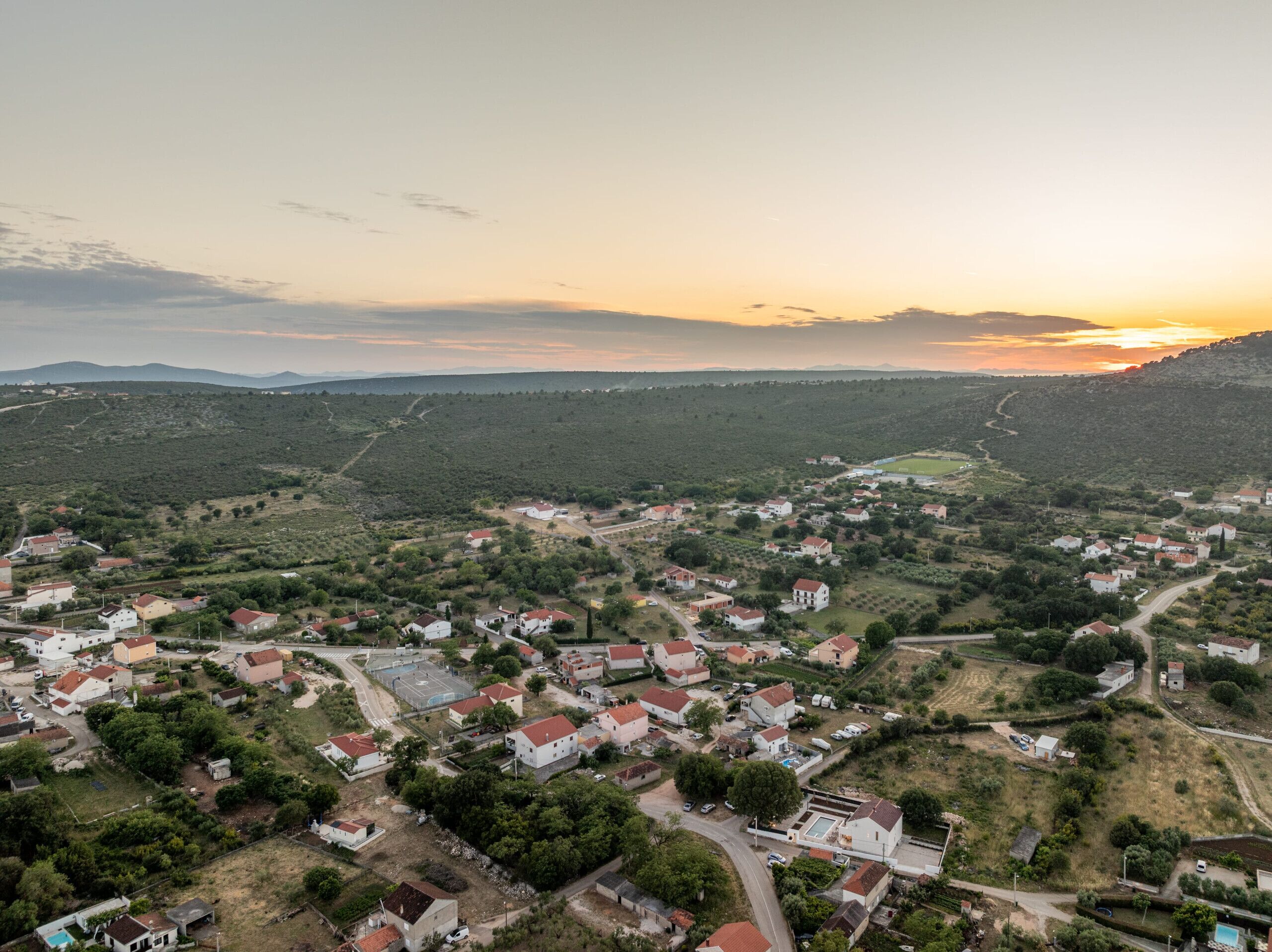 An aerial view of a village with houses, roads, and a large open field.