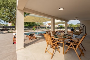 Eine Terrasse im Freien mit Pool, Holzmöbeln und Sonnenschirmen.