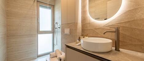 A modern bathroom with a large mirror, a round sink, and a shower.