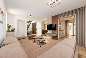 Ein modernes Wohnzimmer mit einer Eckcouch, einem runden Couchtisch, einem Flachbildfernseher und einer Treppe, die zu einer weiteren Ebene führt.