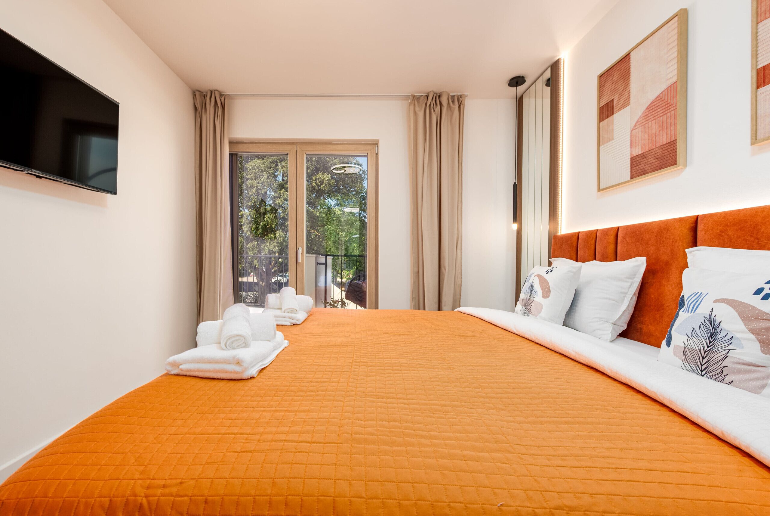 Quarto de hotel com uma cama grande, televisão de tela plana, varanda com cortinas e vista para o verde.