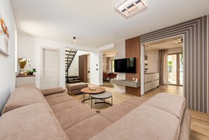 Ein modernes Wohnzimmer mit einer Eckcouch, einem runden Couchtisch, einem Flachbildfernseher und einer Treppe, die zu einer weiteren Ebene führt.