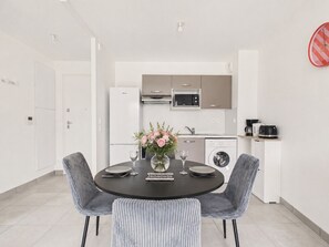 A modern kitchen with white appliances, a dining table with chairs, and a vase with flowers. - 950m from the beach, apartment for 2 (Le Pouliguen)