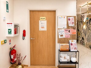 Un espace d’accueil doté d’une porte en bois, d’un équipement de sécurité, d’un extincteur et d’un panneau d’affichage où sont affichés divers avis.