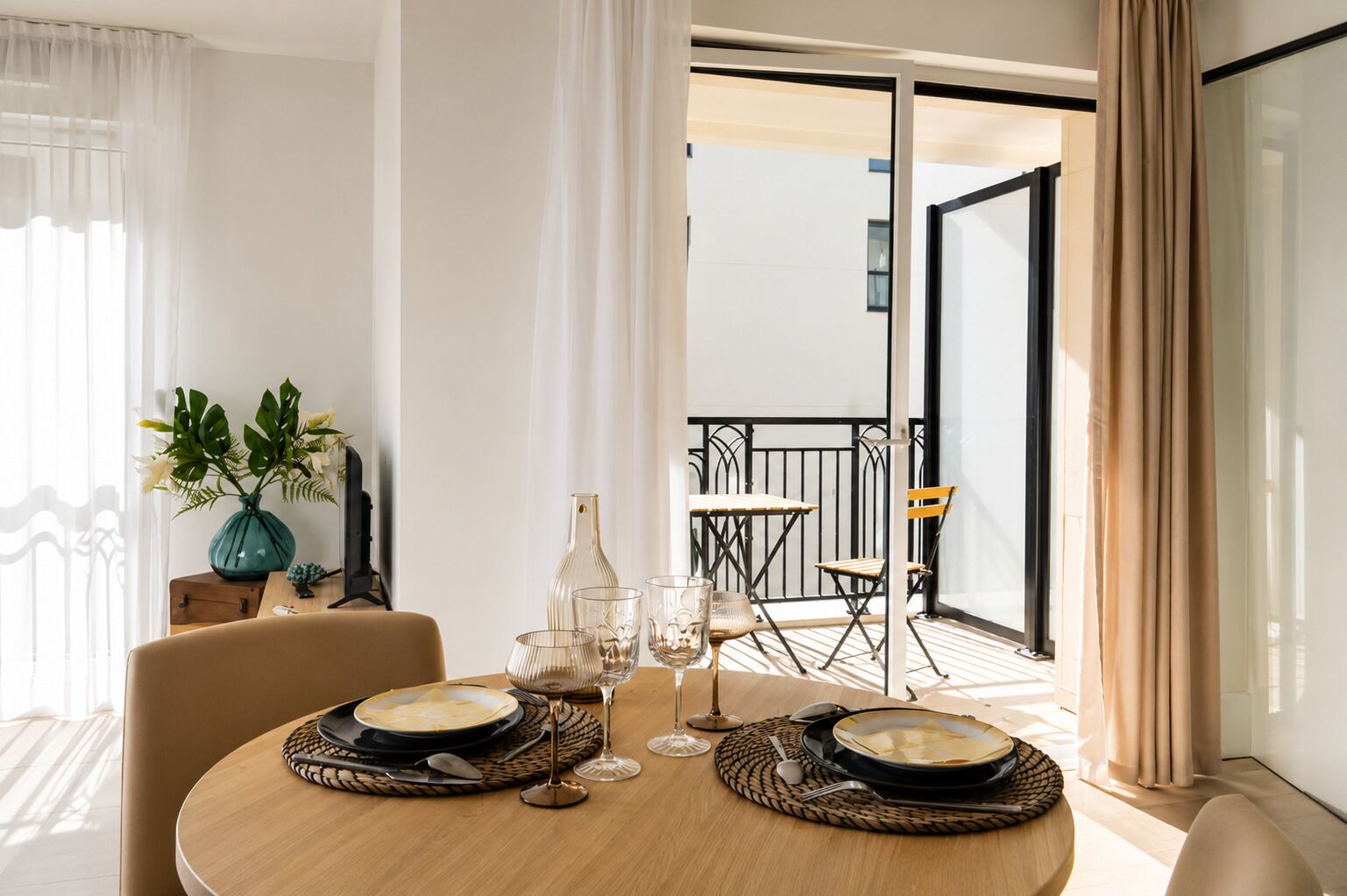 Un'area pranzo con un tavolo rotondo, due sedie, un vaso con fiori e vista su un balcone esterno.