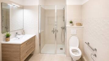 Un baño moderno con ducha envuelta en vidrio, inodoro blanco, tocador de madera con espejo y una planta pequeña en la encimera.