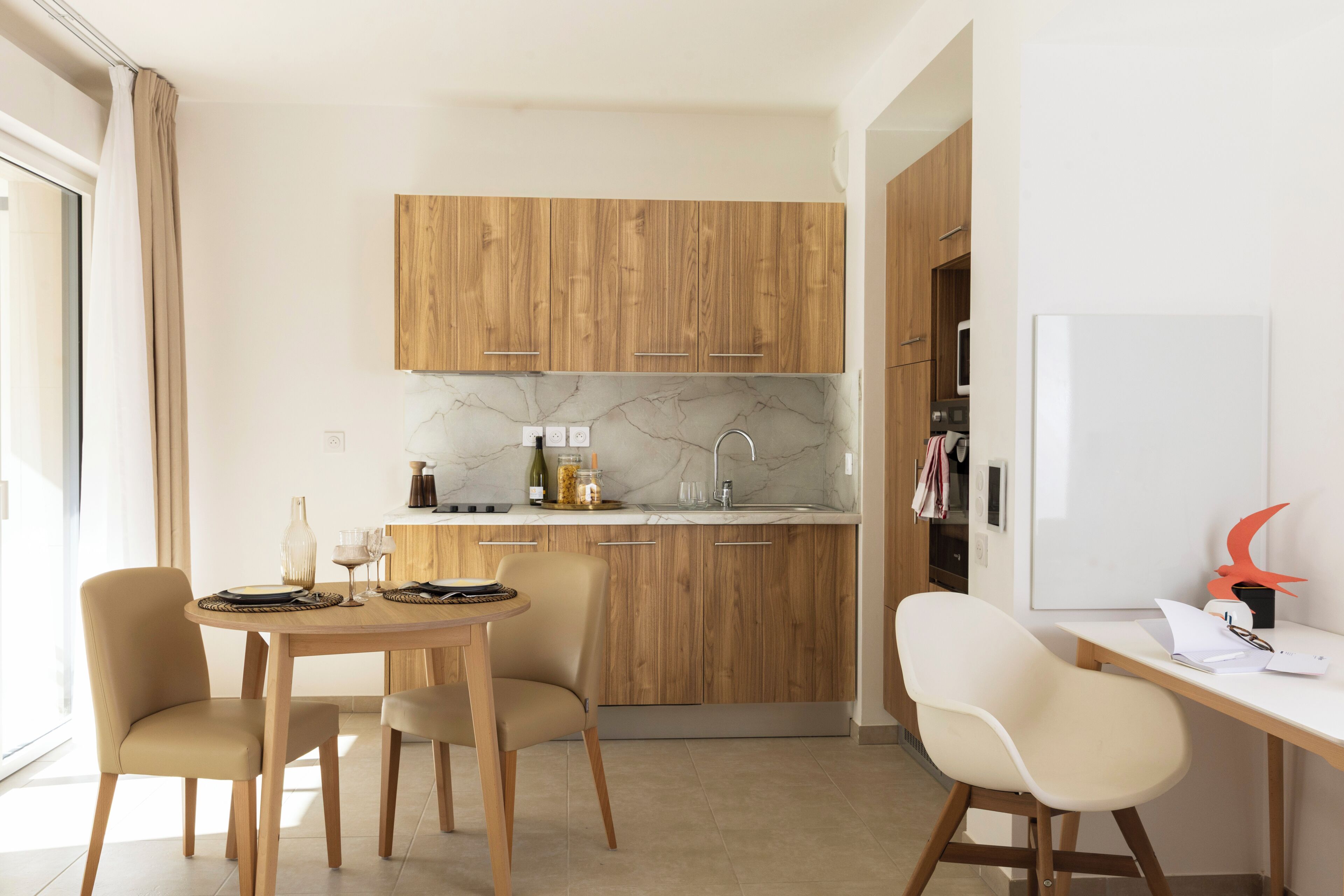 A modern kitchen with wooden cabinets, a marble countertop, and a dining area with a table and chairs.