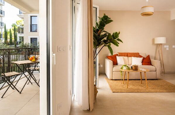 A modern apartment with a balcony, a sofa, a coffee table, and a large plant. - Zenao Appart'hôtels Aix Rambot (Aix-en-Provence)